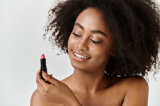 Chanel Ruj Neden Ruh Halimizi Değiştirir? Lüksün Psikolojisi Chanel Rouge Coco Shirtless black woman laughing while posing with lipstick A beautiful young African American woman with curly hair holds a lipstick in her hand, embodying a skin care concept.