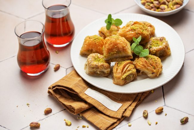 baklava soğuk baklava baklava çeşitleri Turkish sweets with pistachio - baklava Pieces of oriental sweets with pistachios in a white plate on a white ground surrounded by silver and copper utensils